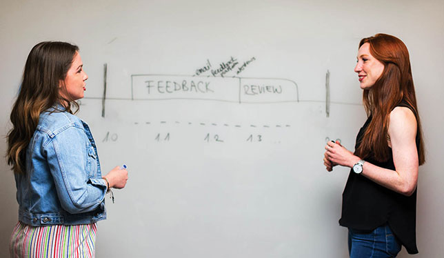 Two women talking in front of a white board