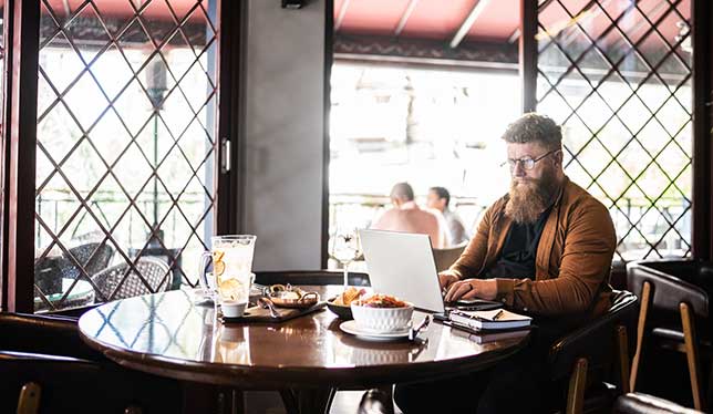 Man sitting at a cafe by himself, working on a laptop